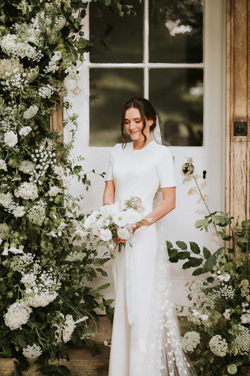 Bride standing infront of entrance door to Aswarby Rectory surrounded by floral arrangement. Photo ©Rosie Kelly Photography