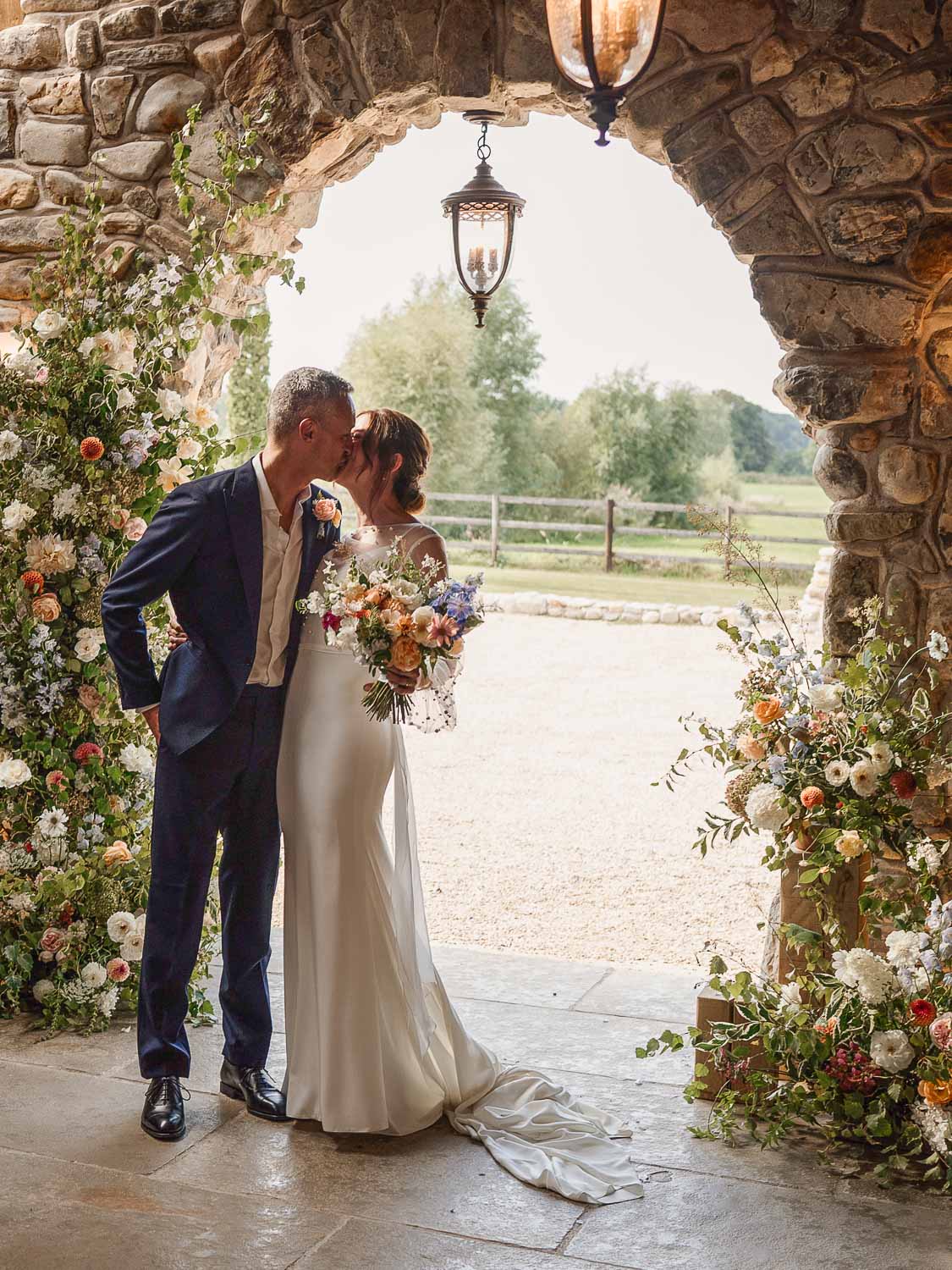 Bride and groom kissing surrounded by floral arrangements in Willow Marsh Farm. Photo ©Magda K