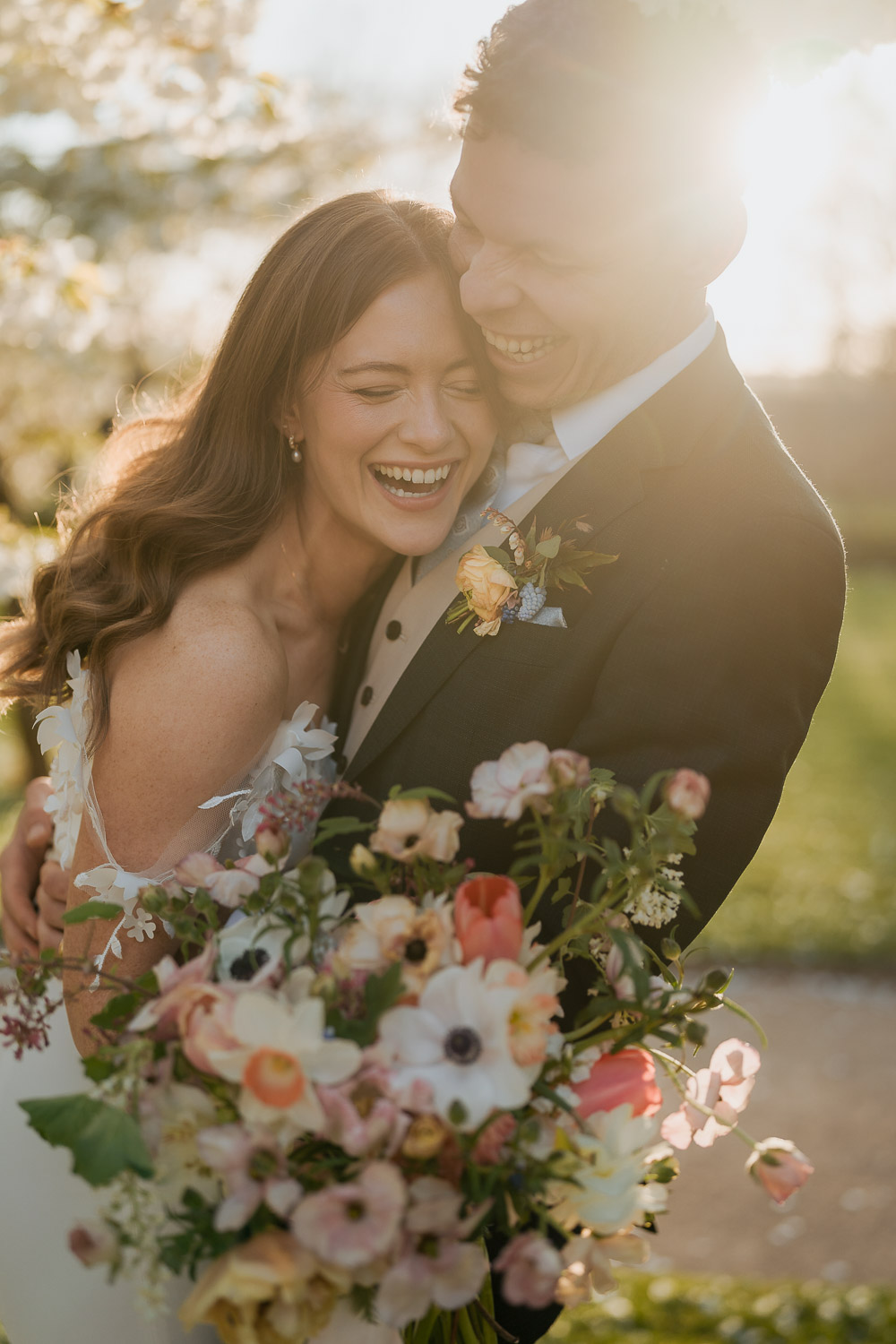 Bride and groom hugging and laughing holding bouquet. Photo ©Bloom Weddings